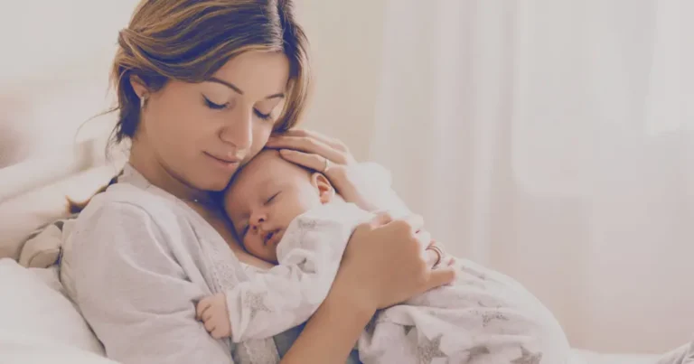 Mother cuddling sleeping baby on bed.